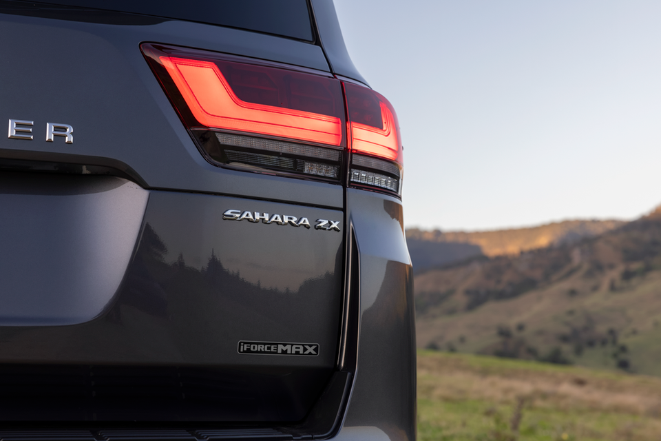 Close-up of the rear quarter panel of a Toyota LandCruiser 300 Sahara ZX with iForce Max badge and tail light, set against an outdoor landscape.