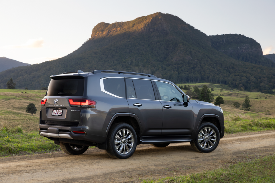 A grey Toyota LandCruiser 300 Series Sahara ZX SUV seen from the rear three-quarter angle on a dirt road with a mountain backdrop