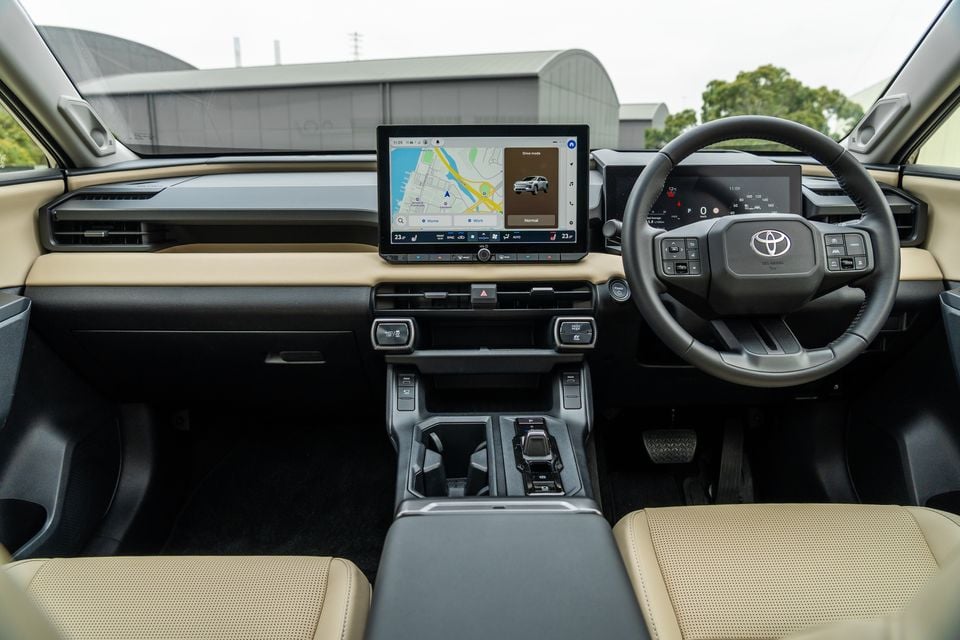 The interior of a 2026 Toyota RAV4 Cruiser shows the dashboard, steering wheel and infotainment screen with a cream and black colour scheme.