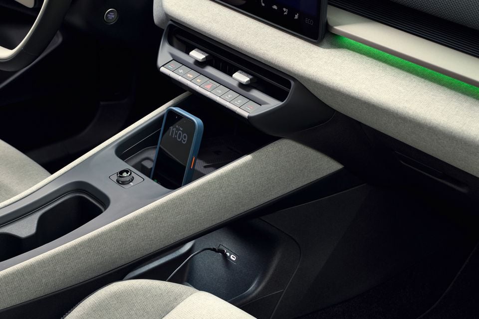 Console central interno do Volkswagen ID.Cross 2026 mostrando um smartphone na bandeja de carregamento sem fio, controles de temperatura e iluminação ambiente verde no painel