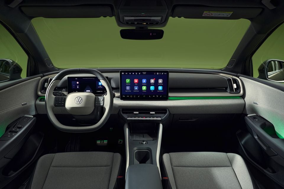 Interior de um Volkswagen ID. Cruz mostrando o painel, grande display central de infoentretenimento com tela sensível ao toque, painel de instrumentos digital, volante e bancos dianteiros com detalhes em iluminação ambiente verde.