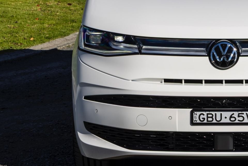 Close-up of the front bumper and headlight of a white 2026 Volkswagen Multivan, showing the VW badge, LED headlight, and front grille with a NSW number plate.