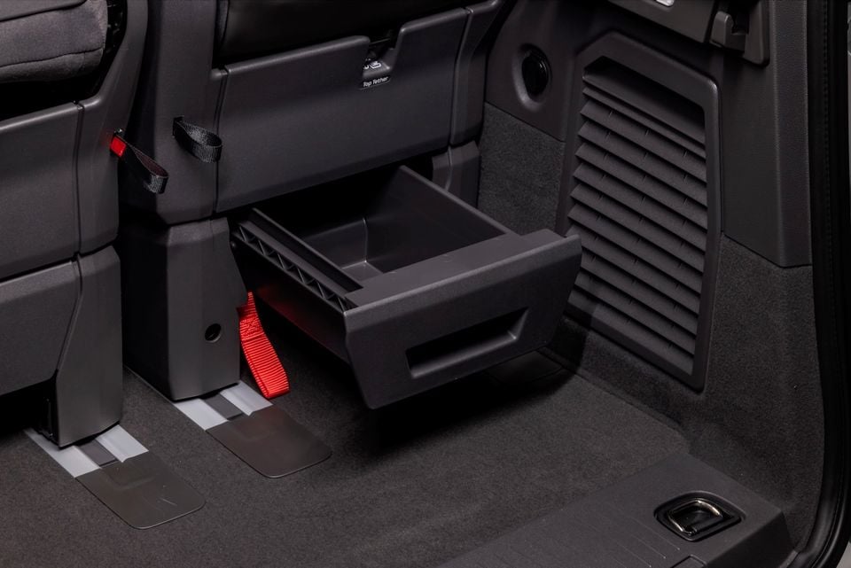 Under-seat storage drawer pulled open in the boot area of a 2026 Volkswagen Multivan, showing a built-in pull-out tray with red seatbelt and top tether anchor points visible