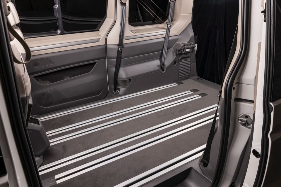 Interior cargo area of a 2026 Volkswagen Multivan with sliding door open, showing a flat load floor with aluminium rails and seat belt anchors