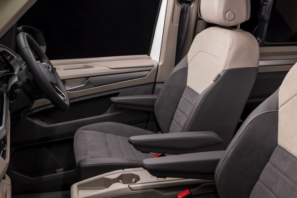 Interior of a 2026 Volkswagen Multivan Edition showing the front seats with two-tone dark grey and cream upholstery, steering wheel, and door trim