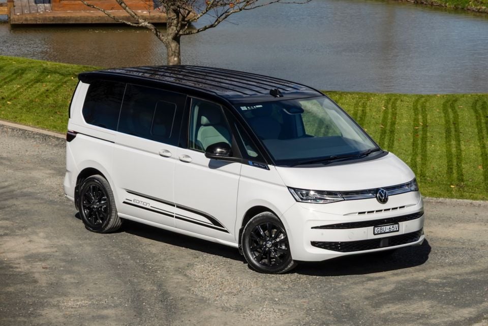 A white 2026 Volkswagen Multivan Edition van seen from the front-side, parked near a waterway