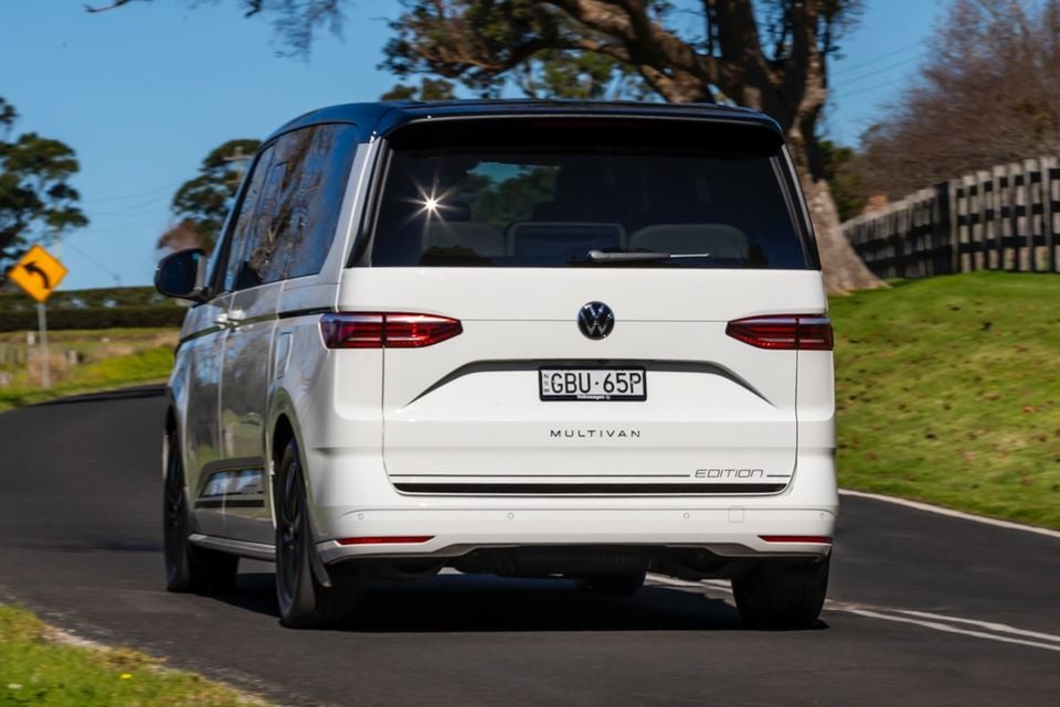 Rear view of a white 2026 Volkswagen Multivan Edition driving on a country road