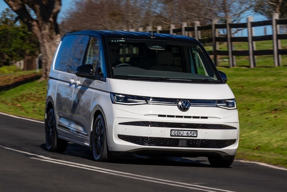 A white 2026 Volkswagen Multivan Edition driving along a rural road, seen from the front