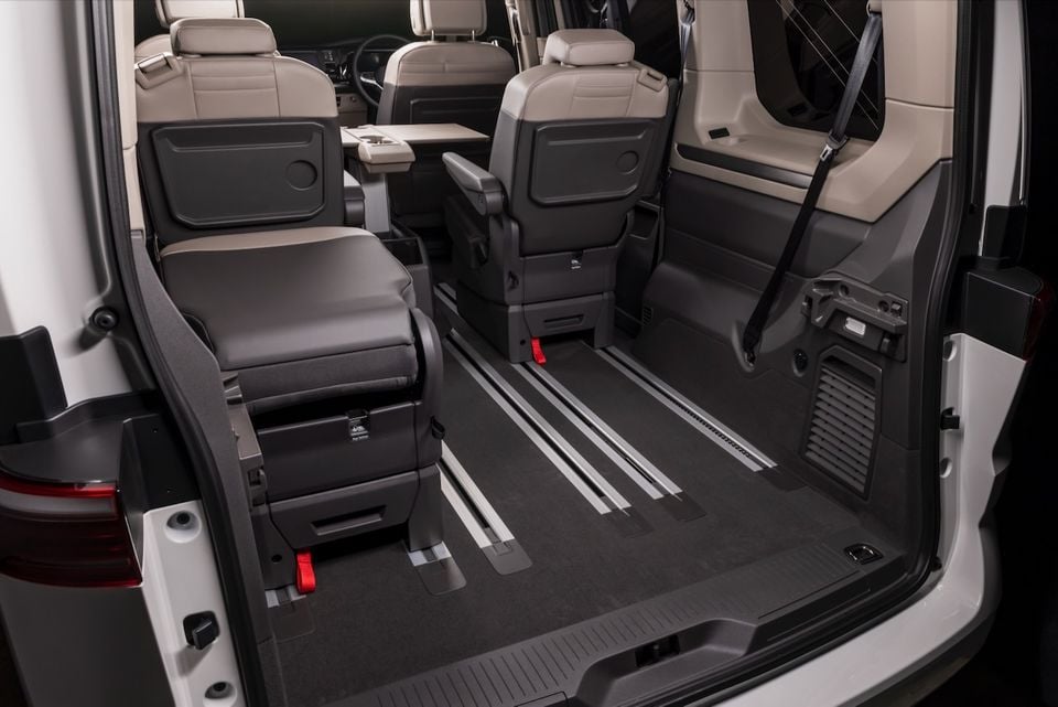 Interior of a 2026 Volkswagen Multivan showing the rear cargo area with flexible seating on floor-mounted rails, viewed from the open tailgate