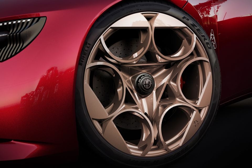 Close-up of the bronze five-hole alloy wheel and Pirelli P Zero tyre on a red 2026 Alfa Romeo 33 Stradale Cuore Rosso, with a carbon-ceramic brake disc behind