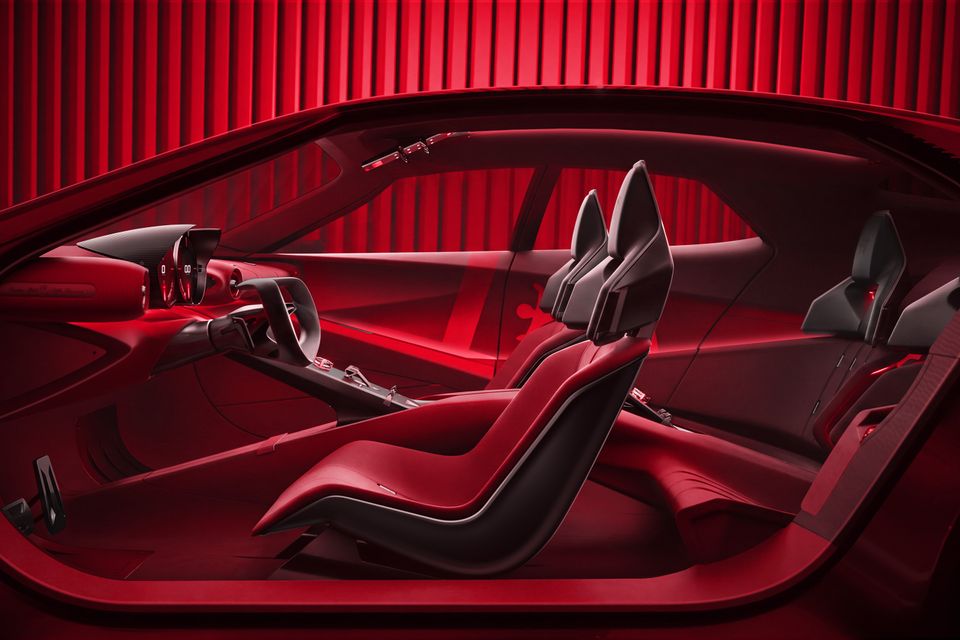 Red cabin of the 2026 Alfa Romeo Cuorerosso concept seen from the side, showing sculpted bucket seats, a yoke-style steering wheel and digital instruments