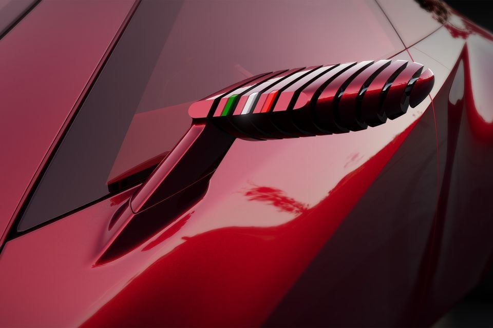 Close-up of the sculpted side mirror on a red 2026 Alfa Romeo Cuorerosso, with Italian tricolour accents on its ribbed housing