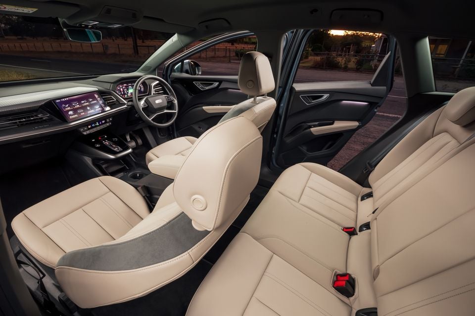 Interior of a 2026 Audi Q4 e-tron showing cream leather seats, dashboard, steering wheel, and touchscreen infotainment system, viewed from the rear door opening