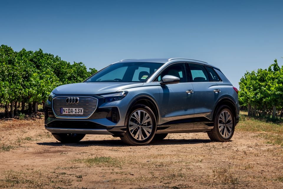 A blue Audi Q4 e-tron SUV parked on a dirt path beside a vineyard, seen from the front-side angle