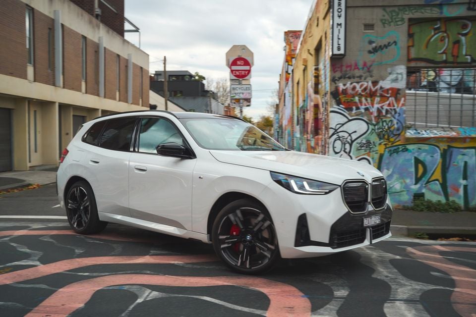 A white 2026 BMW X3 SUV seen from the front-side angle, parked in a graffiti-lined laneway in Australia