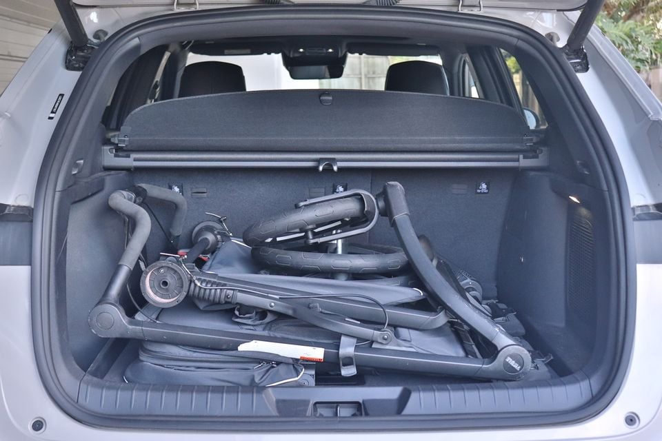 The open boot of a silver 2026 BYD Sealion 6 SUV holding a folded pram, with the cargo cover in place behind it