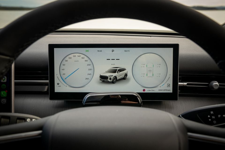 The digital instrument cluster of a Chery Tiggo 9 viewed through the steering wheel, showing a widescreen display with speedometer, vehicle graphic, and tyre pressure readout.