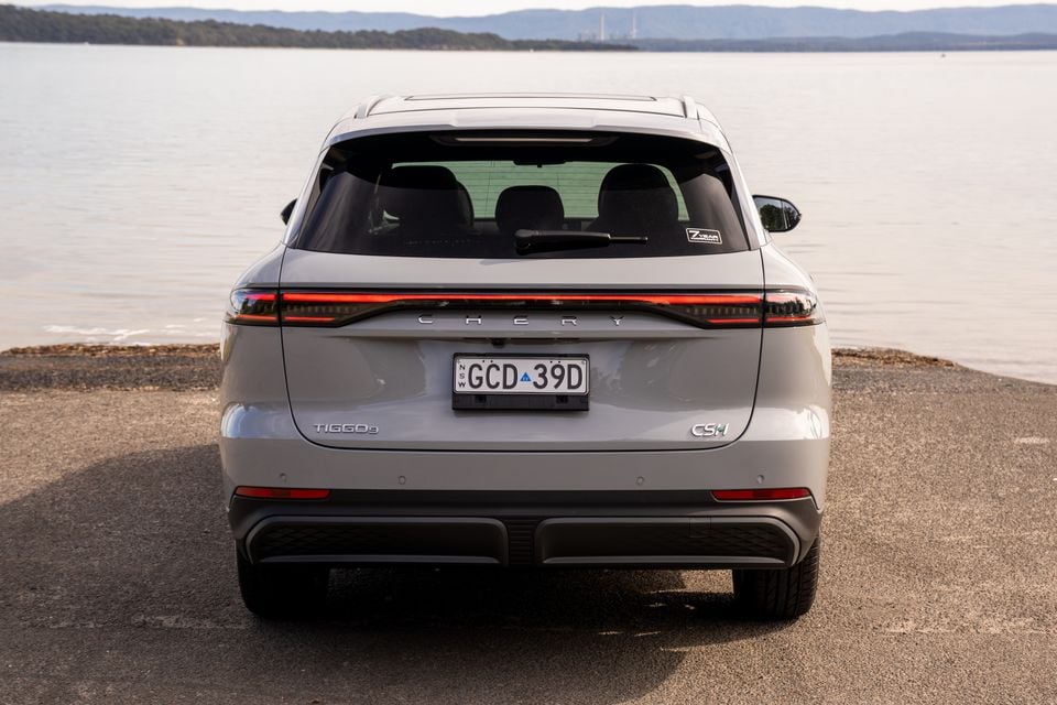 Rear view of a grey Chery Tiggo 9 CSH SUV parked beside a waterway, showing its full-width tail-light bar and badging