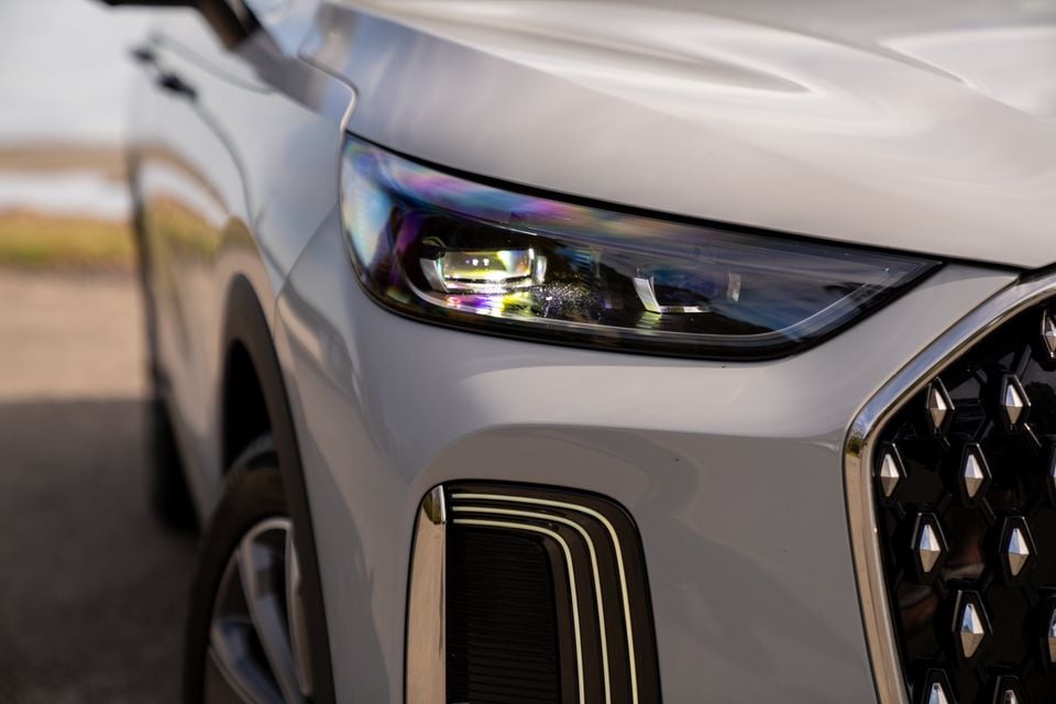 Close-up of the front headlight and grille of a white 2026 Chery Tiggo 9, showing the iridescent LED headlight unit and diamond-pattern grille.