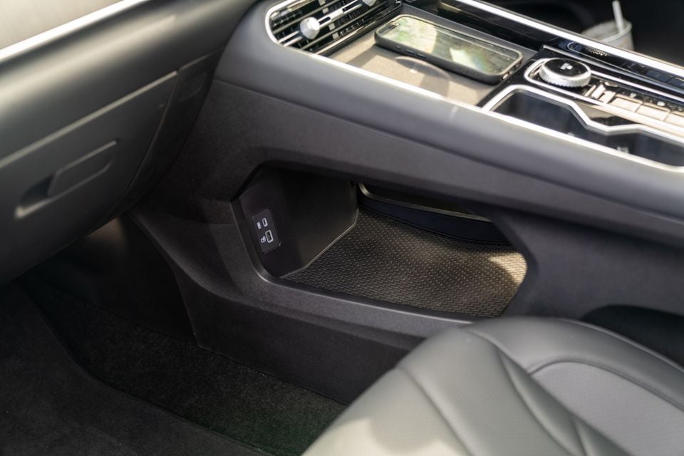 Interior view of a car's centre console area showing a storage compartment with USB ports and a textured mat, with the centre stack controls visible above
