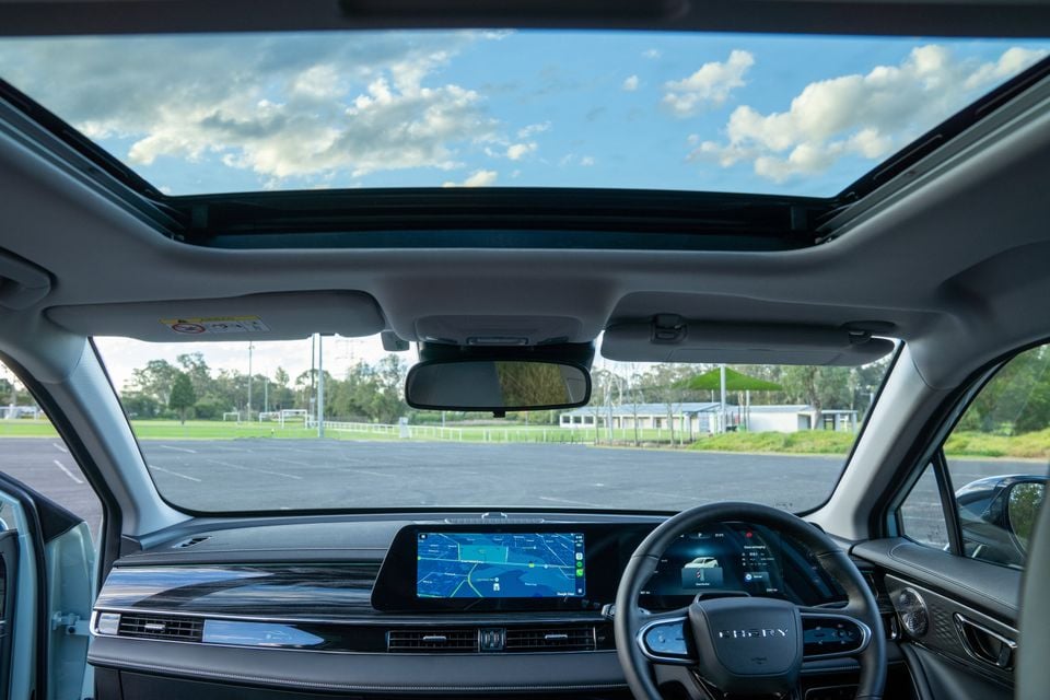 Interior view of a Chery E5 showing the dashboard, central infotainment touchscreen displaying navigation, digital instrument cluster, steering wheel, and a large panoramic sunroof overhead