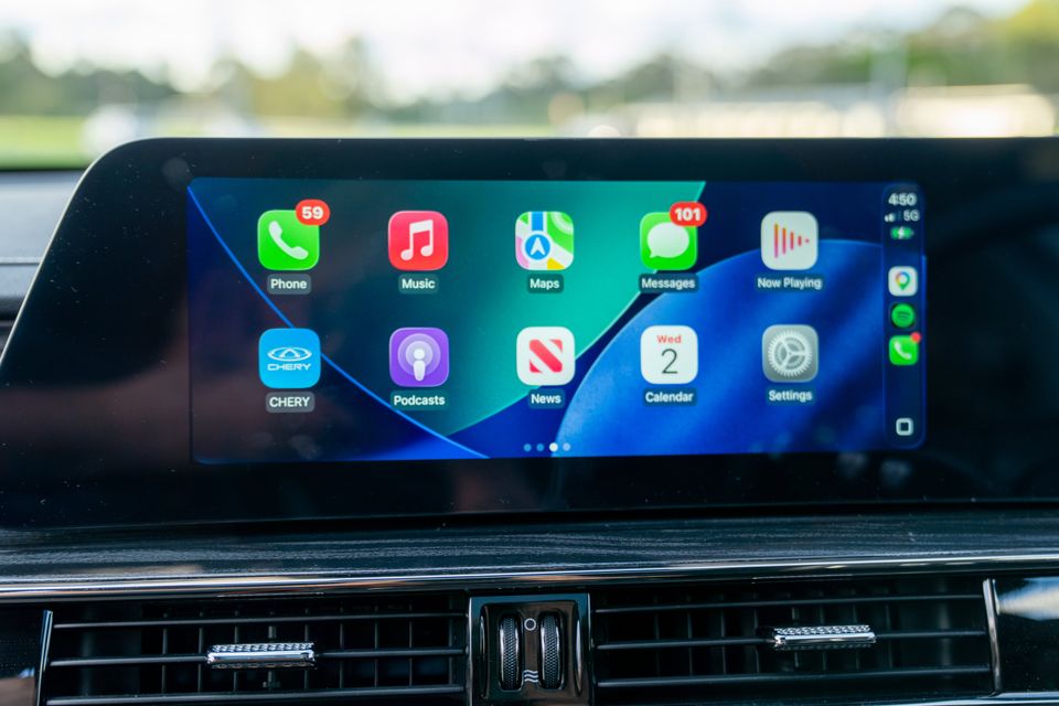 Apple CarPlay interface displayed on the infotainment touchscreen of a Chery E5, showing apps including Phone, Music, Maps, Messages, Podcasts, News, Calendar and Settings