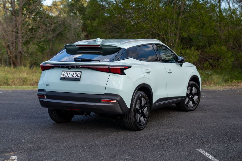 A white Chery E5 SUV seen from the rear three-quarter angle, parked on a road surrounded by trees