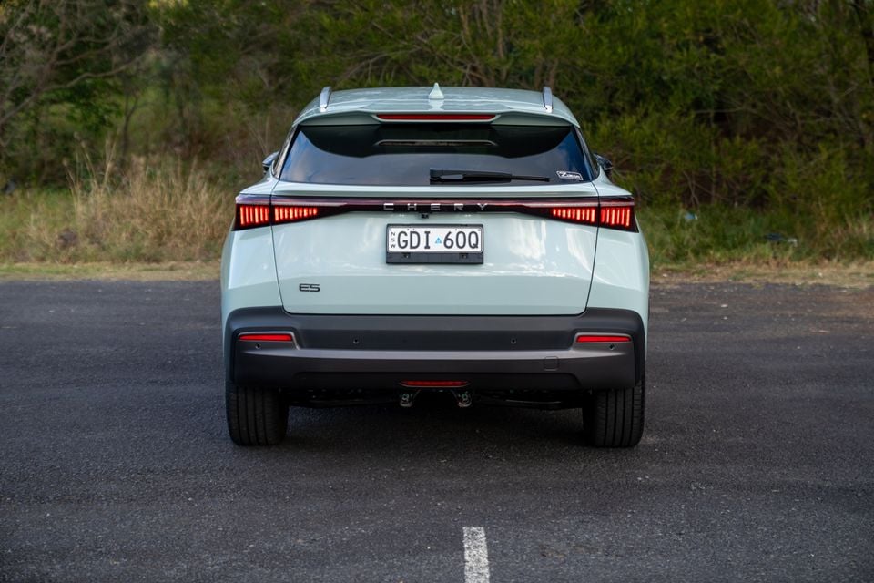 Rear view of a light green 2026 Chery E5 SUV parked on a road with bushland in the background