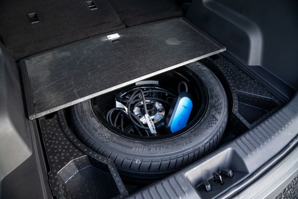 Under-floor storage compartment in a car boot showing a spare wheel with a charging cable and blue EV charger stored inside