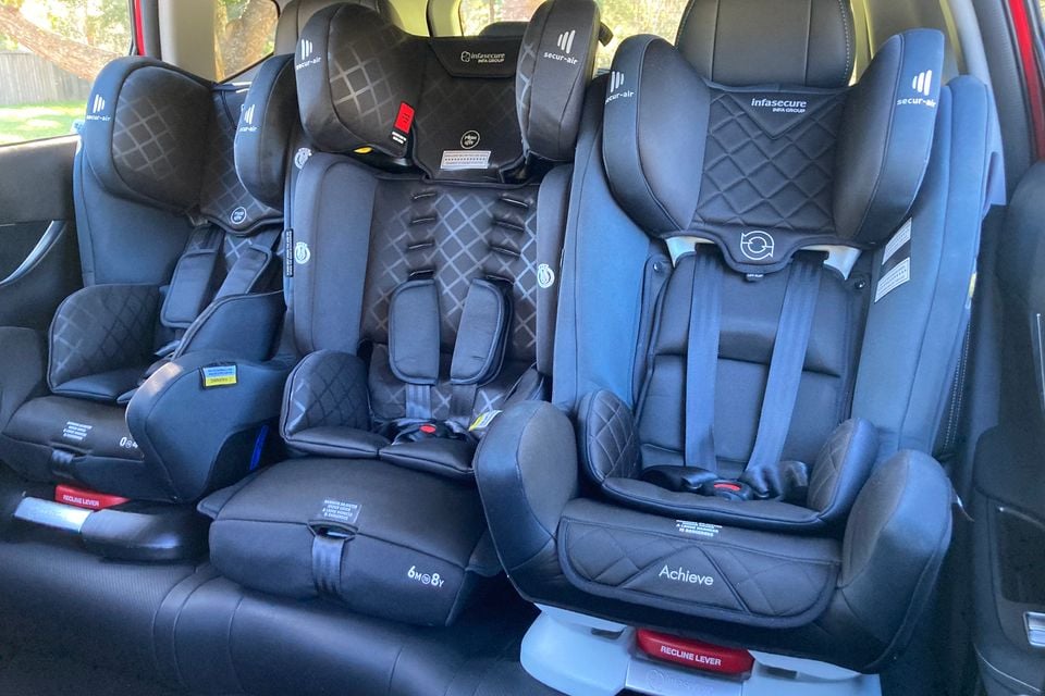 Three black child car seats installed across the rear bench seat of a vehicle, seen from inside the cabin
