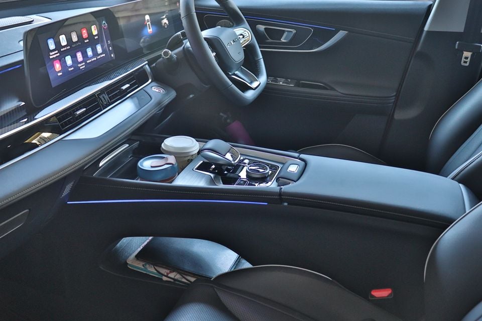 The dark interior of a 2026 Chery Tiggo shows the centre console with cup holders, rotary dial controller, and touchscreen infotainment display.