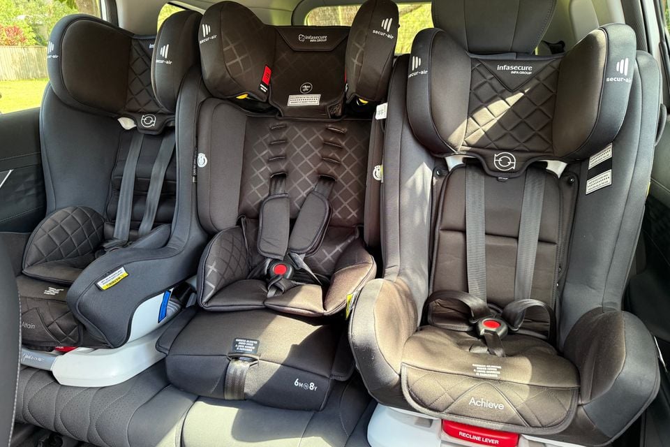 Three child car seats installed across the rear bench seat of a vehicle, seen from inside the cabin