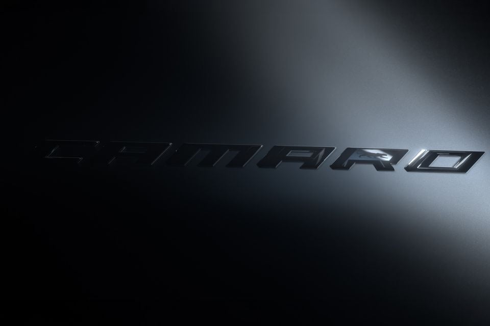 Close-up of the Camaro lettering badge on a 2026 Chevrolet Camaro, dramatically lit against a dark background