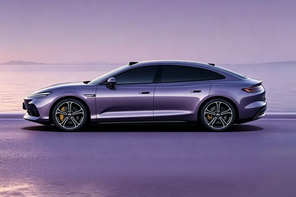 A purple 2026 Denza Z9S fastback sedan seen from the side, with yellow brake calipers and stylish alloy wheels, set against a purple-hued coastal backdrop.