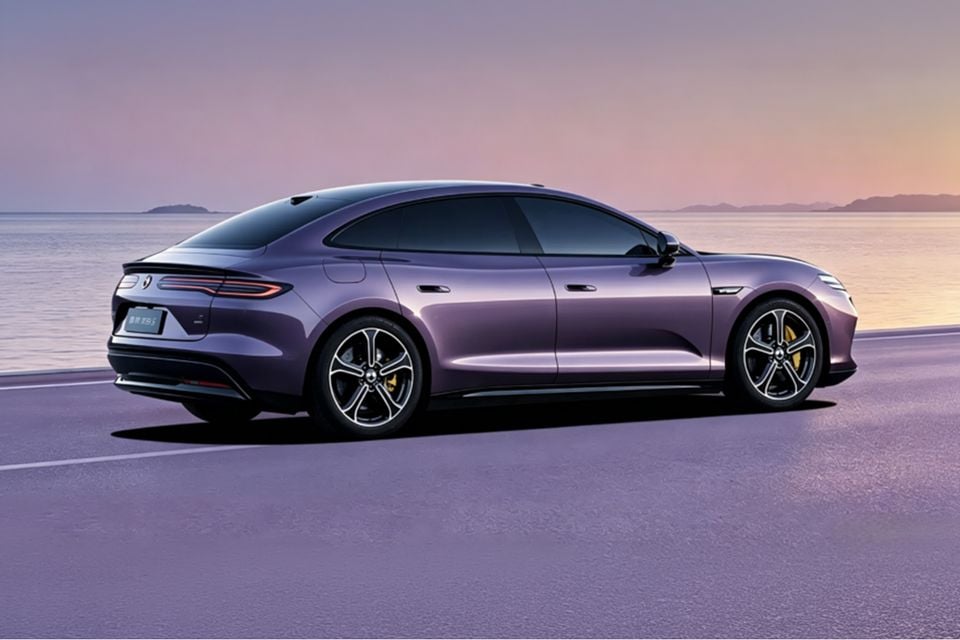 A purple 2026 Denza Z9S fastback sedan seen from the rear three-quarter angle, parked by a waterfront at sunset.
