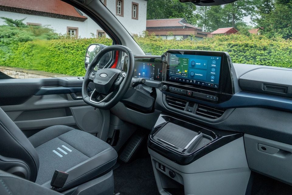Interior view of a Ford Tourneo Custom showing the dashboard, steering wheel, large central touchscreen infotainment display, and front seats