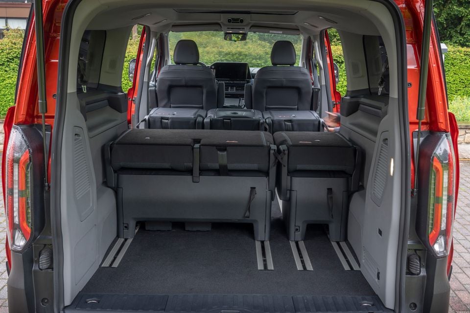 Interior boot area of a red 2026 Ford Tourneo Custom van, viewed from the rear with the tailgate open, showing folded second-row seats and a large flat cargo floor