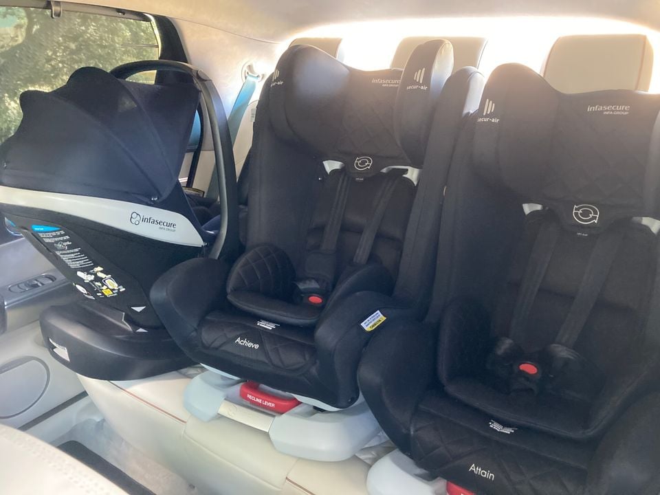 Three Infasecure child car seats — including an infant carrier and two convertible seats labelled Achieve and Attain — fitted across the rear seats of a vehicle