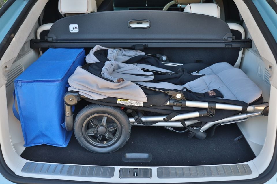 The boot of a Genesis GV60 SUV loaded with a folded pram and a blue bag, with a cargo blind in place