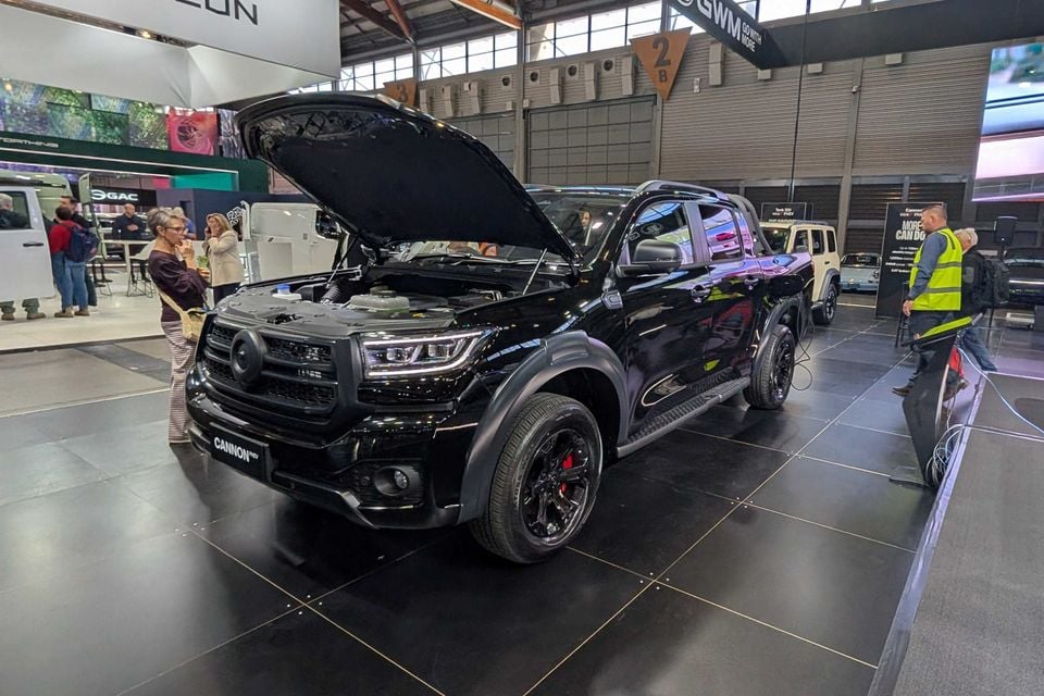 A black 2026 GWM Cannon PHEV ute on display at a motor show with its bonnet open, showing the engine bay