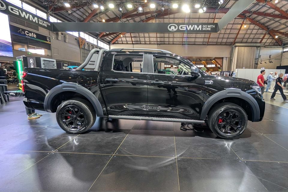 A black 2026 GWM Cannon PHEV dual-cab ute on display at a motor show, seen from the side.
