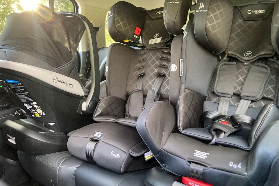 Three child car seats, including an InfaSecure infant capsule and two convertible seats, fitted across the rear row of a vehicle, likely a GWM Tank 300 PHEV.