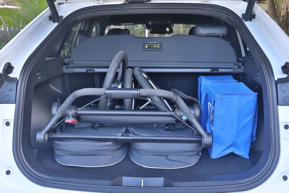 Open boot of a white 2026 Haval H6 GT holding a folded twin pram and a blue storage bag, with the cargo cover in place