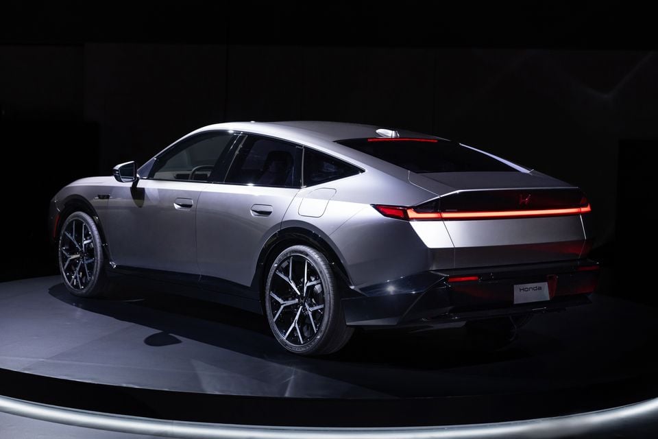 A silver Honda hybrid sedan prototype seen from the rear three-quarter angle on a dark studio display platform