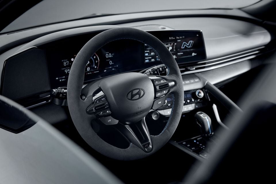 Dashboard of the 2026 Hyundai i30 Sedan N with a suede steering wheel, curved digital instrument and infotainment displays, and gear selector