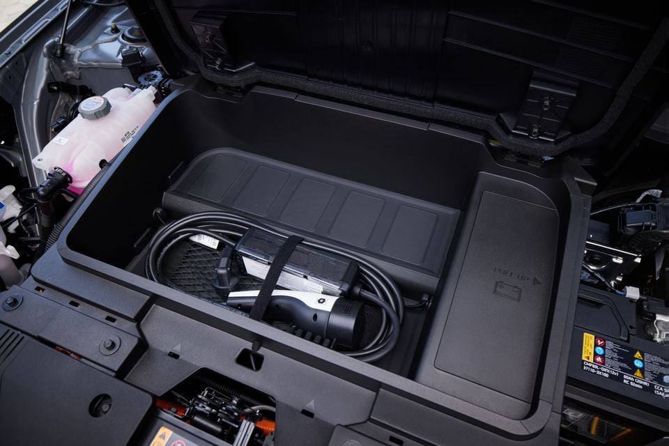 The front trunk (frunk) of a 2026 Hyundai Kona Electric, showing a charging cable storage compartment under the bonnet.