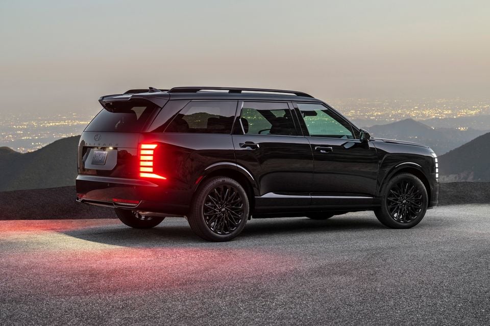 A black 2026 Hyundai Palisade large SUV seen from the rear three-quarter angle at dusk, with city lights visible in the background and LED tail lights illuminated.