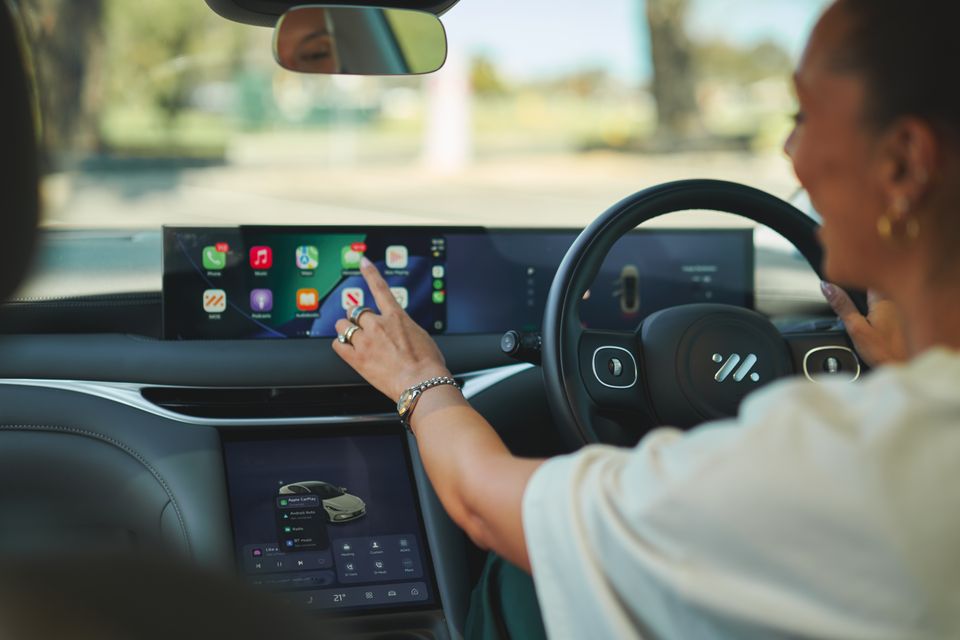 Um motorista toca a tela do Apple CarPlay no painel de um IM5 2026, com uma tela sensível ao toque inferior mostrando controles de clima e mídia