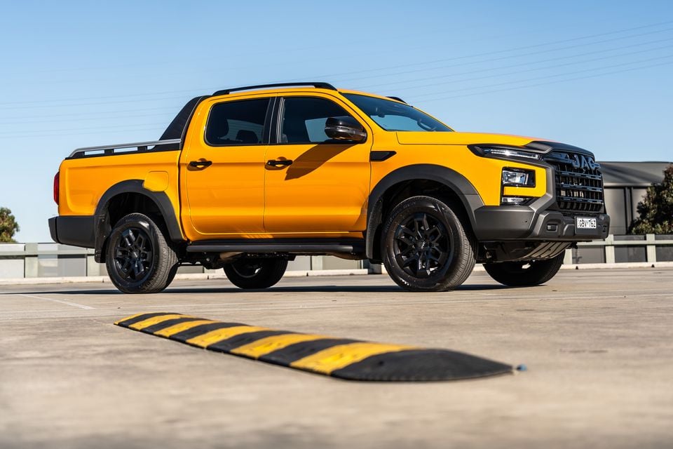 A yellow JAC Hunter dual-cab ute seen from the front-side angle in a car park, with a speed bump in the foreground