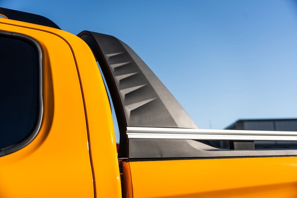 Close-up of the rear cab corner and canopy spoiler on a yellow JAC Hunter PHEV ute, showing textured dark plastic trim and chrome rail detail against a blue sky